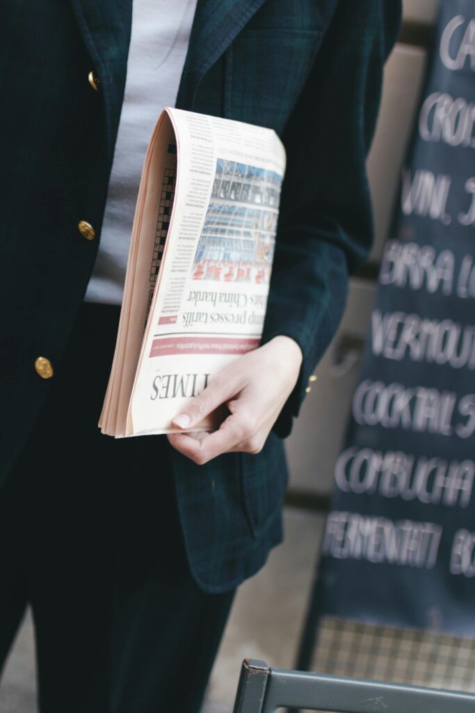 A business person in a suit holding a rolled-up newspaper outside a cafe.